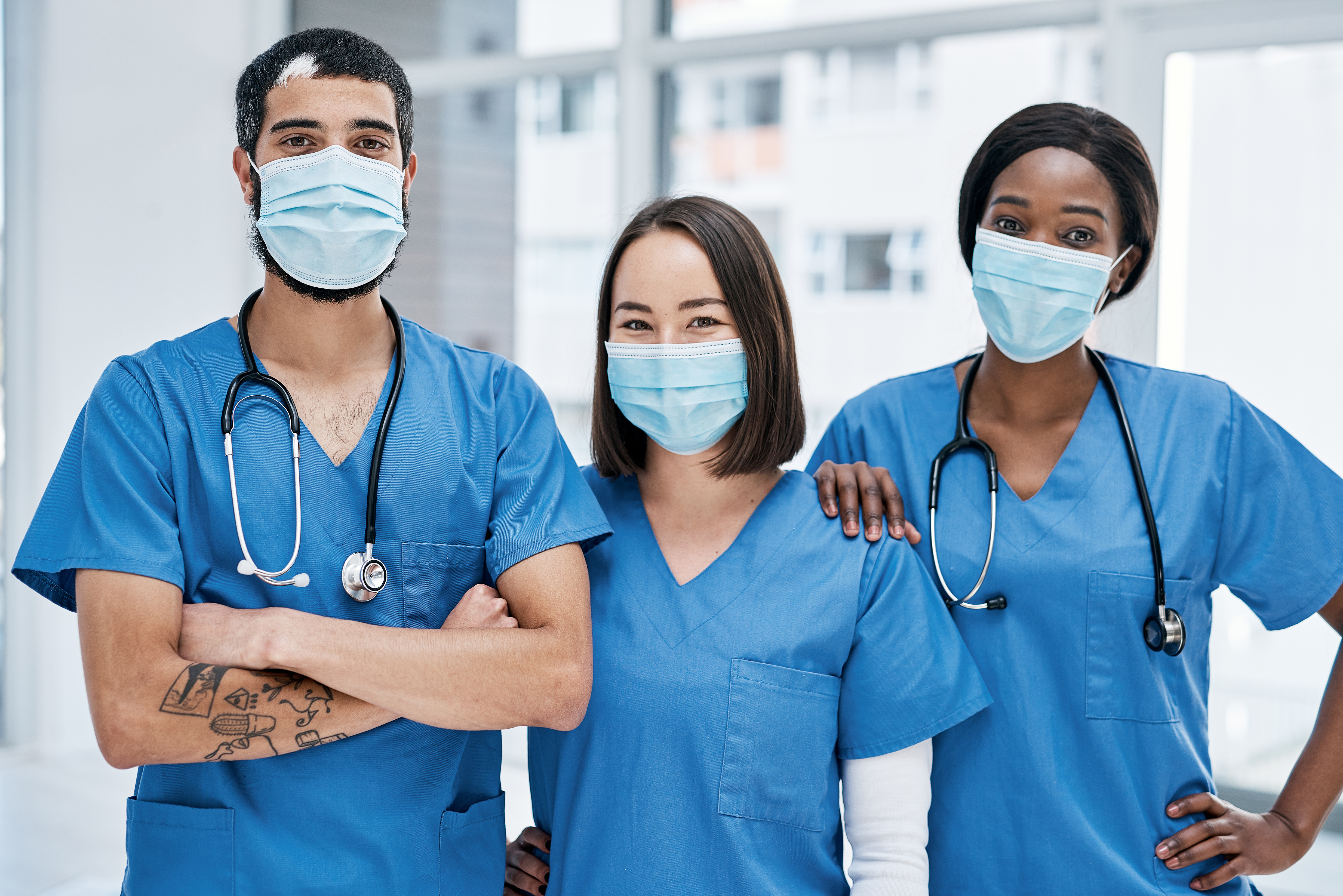 Three nurses wearing blue scrubs and masks