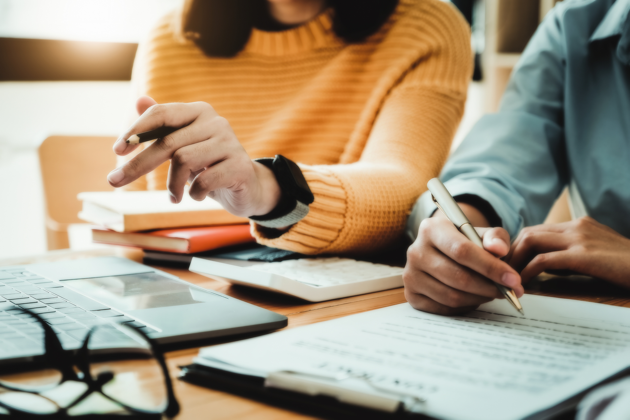 Two people holding pens and writing on a notepad 