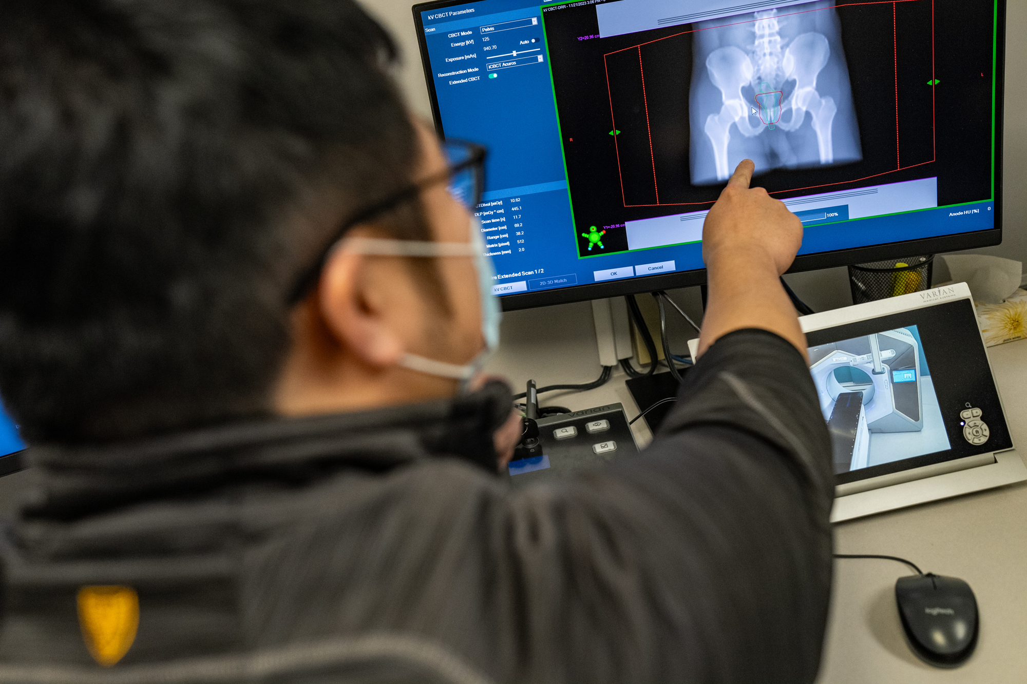 A technician pointing at an MRI scan on a computer screen