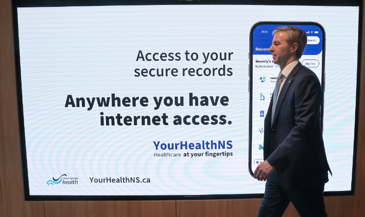 premier houston walks by a a screen with health records information on it. 