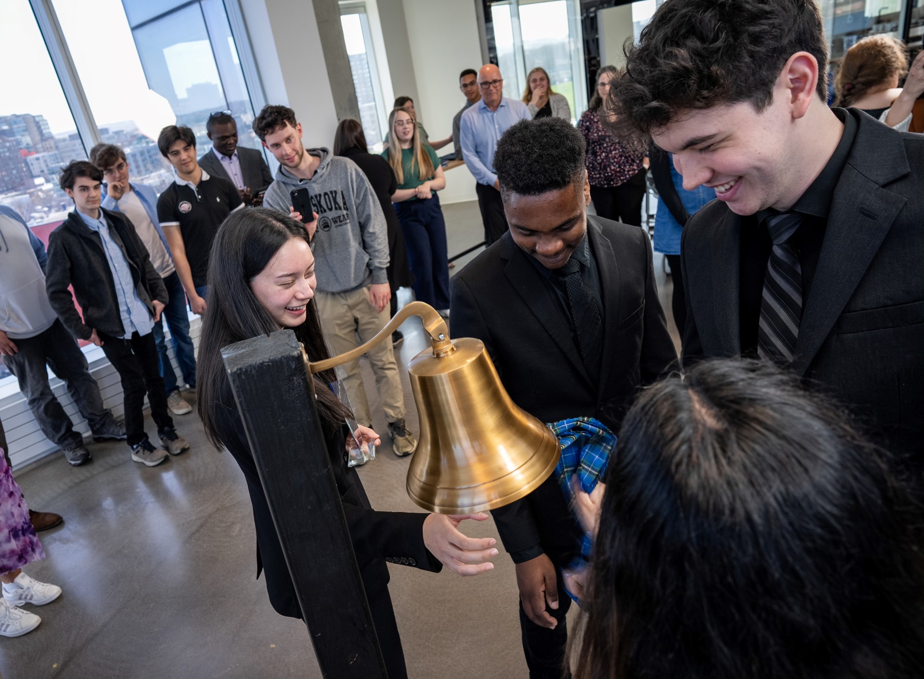 Four young people smile while ringing a bell with a piece of tartan at the Nova Scotia Health Innovation Hub. 