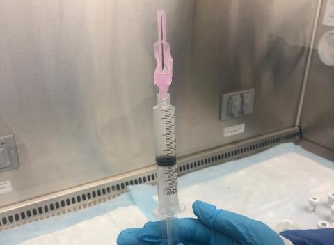 A person wearing blue gloves holds up a syringe containing donated genetically engineered CAR T-cells.