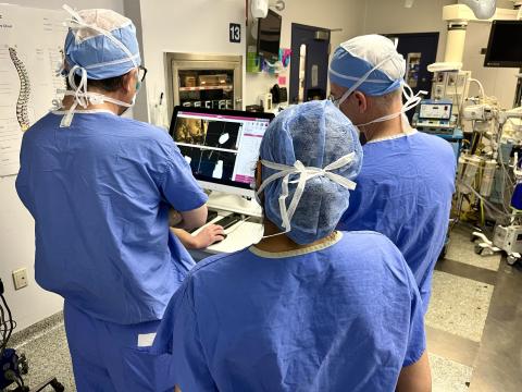 Surgeons dressed in blue scrubs look at the screen of a surgical robot that is mapping out an operation to insert electrodes in a patient's brain.