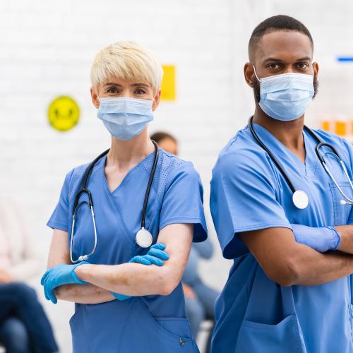 Two nurses wearing masks, arms crossed.