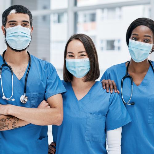 Three nurses wearing blue scrubs and masks