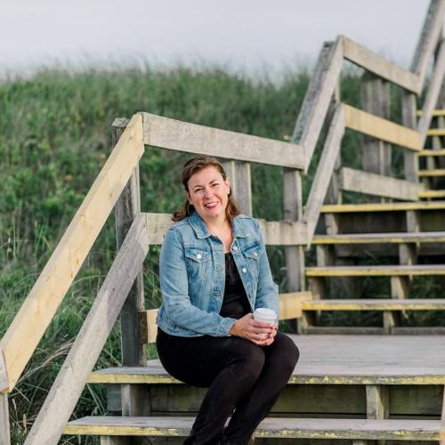 Andrea Van Hal sits on a set of steps, leading to a beach.