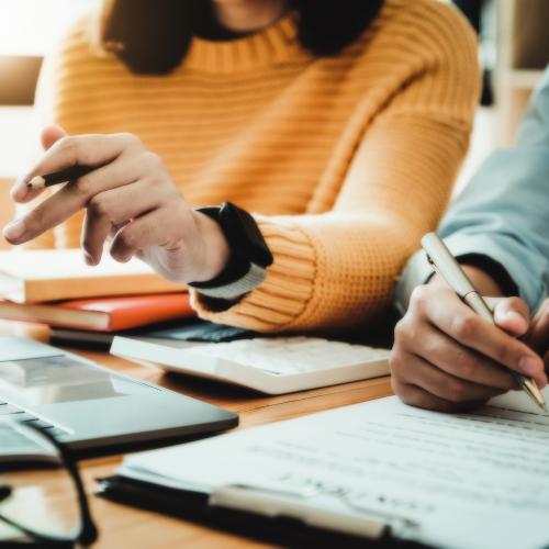 Two people holding pens and writing on a notepad 