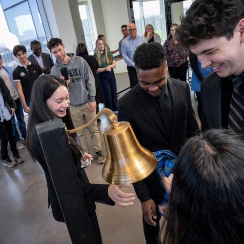 Four young people smile while ringing a bell with a piece of tartan at the Nova Scotia Health Innovation Hub. 