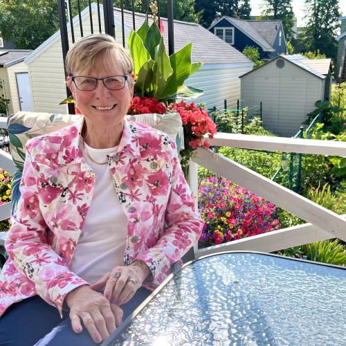 Debbie Purchase smiles at the camera wearing a pink and white floral jacket in her sunny backyard. 